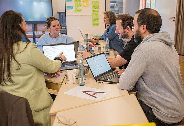Teilnehmende in Coachingworkshop besprechen Inhalte an Laptops